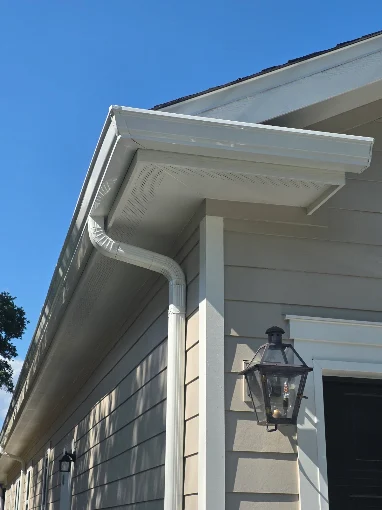 White seamless gutter and downspout fitted to the corner of a light-colored home.